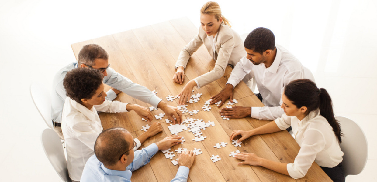 (© © Getty Images/iStockphoto/fotostorm) Menschen sitzen mit Puzzleteilen vor einem Tisch