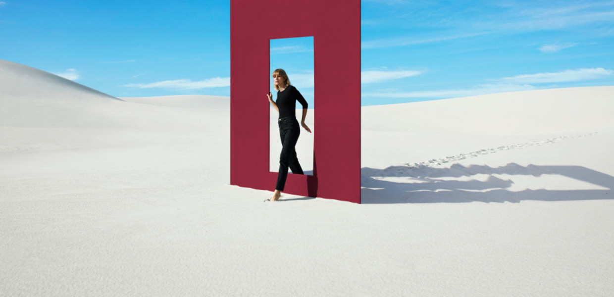 (© © Getty Images / DigitalVision / Klaus Vedfelt) Frau geht durch Tür, auf Sand mit blauem Himmel